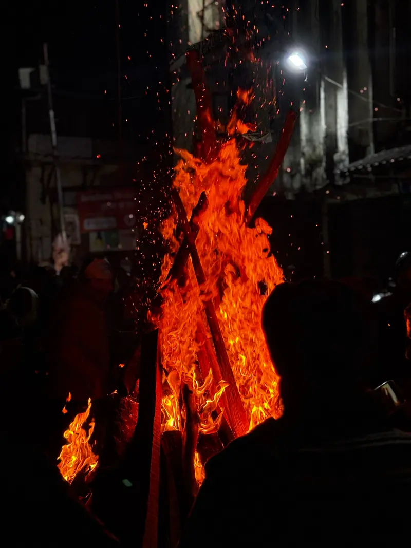 Towering Lohri festival bonfire with embers and sparks shooting into the night sky near Landour.