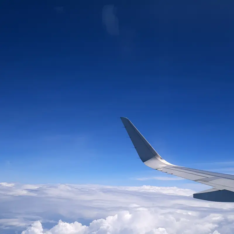 Airplane winglet rising above fluffy white clouds under deep blue stratosphere.