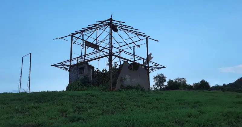 Abandoned metal pavilion structure perched on a grassy hill knoll.